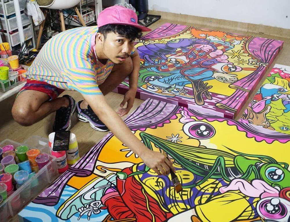 Muklay sedang menggoreskan kuas di atas kanvas yang dipenuhi lukisan warna-warni